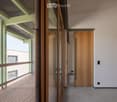 Modern hallway with wooden doors, glass partitions, and a view onto a wooden decked balcony area.