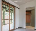 Empty room with white walls, light wooden ceiling, large sliding glass door leading to a balcony, and a built-in wooden closet with shelves.