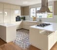 Modern kitchen with light-colored cabinets, white countertops, a gas stove, and a large range hood. Features a central island, wooden flooring, and a decorative tile backsplash.
