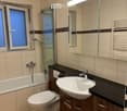 Modern bathroom with a white sink, toilet, bathtub, and a glass-enclosed shower area. Features a large mirror, wooden cabinets, and a window with frosted glass.