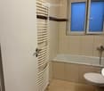 Modern bathroom with beige tiles, a bathtub, toilet, and a white radiator on the wall.