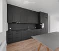 Modern kitchen with dark grey cabinets, a sink, and a grey table with wooden legs.