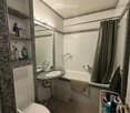 Modern bathroom with white tiles, granite countertop, bathtub, toilet, sink, mirror, and towel rack.