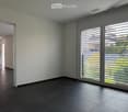 Empty room with dark tiled floor, white walls, large sliding glass doors with blinds, and an open doorway leading to another room.