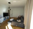 Living room with wooden flooring, grey sectional sofa, coffee table, TV, drawer unit, and floor lamp.
