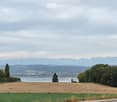 Scenic view of a rural landscape with fields, trees, a body of water, and distant mountains under a cloudy sky.