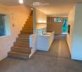 Modern hallway with wooden staircase, white cabinets, and a sink area. Exposed wooden beams on the ceiling and large windows provide natural light.