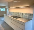 Modern kitchen with stainless steel sink, white cabinets, and a sleek countertop, featuring a large window and minimalist design.