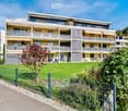 Modern multi-story residential building with balconies, large windows, and a well-maintained lawn in front.