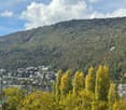 Scenic view of a town nestled in a forested valley, with a lake in the foreground and hills in the background.