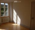 Empty room with wooden flooring, white walls, a window with a radiator below, and a closed door.