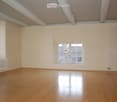Empty room with wooden flooring, white walls, and a single window showing a roof view. Radiators are present on two walls.