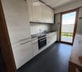 Modern kitchen with white cabinets, black tiled floor, stainless steel oven, sink, and faucet. A sliding glass door leads to a balcony.
