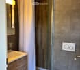 Modern bathroom with a wooden vanity, sink, mirror, toilet, and a glass-enclosed shower with a white curtain.