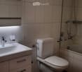 Modern bathroom with a white sink, toilet, and glass-enclosed shower. Features a large mirror with built-in lighting and a sleek faucet.