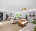 Modern living room with a large sectional sofa, wooden coffee table, dining area with a table and chairs, bookshelf, and several potted plants. The space features large windows and a sleek, contemporary design.