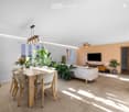 Open-plan living and dining area with a white sofa, wooden dining table with chairs, television, potted plants, and a ceiling fan.