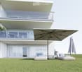 Modern two-story house with balconies, outdoor seating area featuring sun loungers, umbrella, and small table on a grassy lawn.