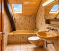 Bathroom with wooden walls and ceiling, featuring a bathtub, toilet, sink, and a mirror with shelves above it. The room has skylight windows and decorative leaf patterns on the tiles.