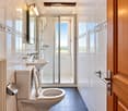 Modern bathroom with white tiles, a toilet, sink, shower, and a large window offering a view of the outdoors.
