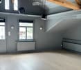 Empty room with exposed wooden beams, grey walls, large windows, and radiators. No furniture or equipment present.