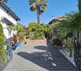A well-maintained garden pathway lined with palm trees, shrubs, and potted plants, leading to a house entrance.