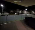 Balcony with glass railing, small table, and view of street with parked vans and residential buildings.