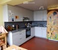 Modern kitchen with white cabinets, dark backsplash, and stainless steel appliances. Includes a sink, oven, refrigerator, and a small table with chairs.