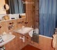 Bathroom with two sinks, a bathtub, a mirror, and a shower curtain. The room features tiled walls and a tiled floor, with various toiletries and a wicker basket on the shelves.