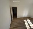 Empty room with light wooden flooring and white walls, featuring an open doorway leading to another room.