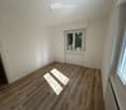 Empty room with light wooden flooring, white walls, and large windows allowing natural light. No furniture or equipment is present.