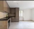 Modern kitchen with light-colored cabinets, a black countertop, and a stainless steel oven. The space is bright with white walls and tiled flooring.