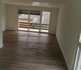 Empty room with wooden flooring, large sliding glass doors leading to a balcony, and white walls.