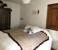 Cozy bedroom with a large bed, patterned pillows, a textured blanket, an antique wardrobe, and a wall-mounted lamp.