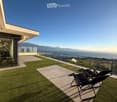 Modern rooftop terrace with artificial grass, sun loungers, and a panoramic view of the sea and mountains.