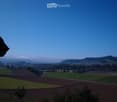 Panoramic view of a rural landscape with fields, scattered trees, and distant hills under a clear blue sky.