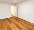 Empty room with light wooden flooring and white walls, featuring an open doorway leading to another space.