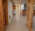 Spacious hallway with wooden beams and tiled floor, leading to a kitchen area with white cabinets and a countertop.