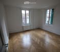 Empty room with wooden herringbone flooring, white walls, and two windows with white frames. A radiator is visible under one window.