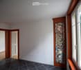Empty hallway with white walls, dark tiled floor, wooden doors, and a colorful abstract painting on one wall.