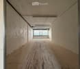 Empty hallway with wooden flooring, white walls, and a single window at the end.