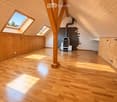 Bright, empty attic space with wooden floors, exposed wooden beams, skylights, and a modern fireplace.