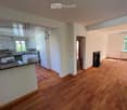 Open-plan living and kitchen area with wooden flooring, white kitchen cabinets, a central island, and a fireplace.