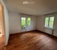 Empty room with wooden flooring, white walls, and large windows allowing natural light. Features a radiator and a door leading to another space.