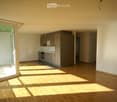 Empty kitchen with wooden flooring, grey cabinets, and a large window letting in natural light.