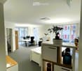 Modern office space with white walls, grey carpet, desks, chairs, computer monitors, and a potted plant on a shelf.