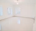 Empty room with white walls, polished white floor, and multiple windows allowing natural light.