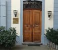 Entrance to a building with a double wooden door, ornate metalwork above, and decorative wall-mounted lanterns on either side.