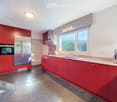Modern kitchen with red cabinets, stainless steel appliances, granite countertop, and large windows.