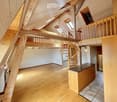 Open-plan attic space with wooden beams, exposed wooden floor, spiral staircase leading to a loft area, and a small kitchen counter with cabinets.